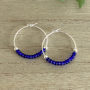 May include: A pair of silver hoop earrings with small blue glass beads.