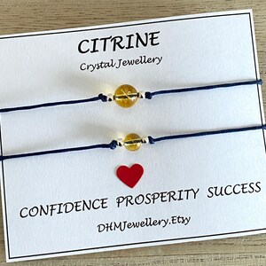 Könnte beinhalten: Zwei blaue Armbänder aus Schnur mit goldenen Perlen und Citrin-Steinen. Die Armbänder befinden sich auf einer weißen Karte mit den Worten "Citrine Crystal Jewellery" und "Confidence Prosperity Success DHMJewellery.Etsy".
