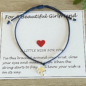 May include: A navy blue string bracelet with a puzzle piece charm, presented on a card with the text "For A Beautiful Girlfriend" and "A Little Wish For You". The card also includes instructions on how to use the bracelet.