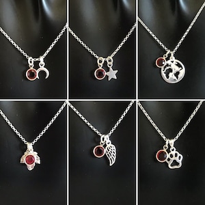 May include: Six silver necklaces with red gemstone charms. Each necklace features a different charm, including a crescent moon, a star, a globe, a leaf, an angel wing, and a paw print.
