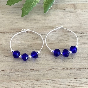 May include: Silver hoop earrings with three blue faceted glass beads on each earring.