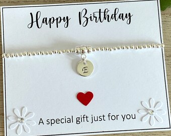 May include: A silver beaded bracelet with a round charm engraved with the letter "E" hangs on a white card. The card reads "Happy Birthday" and "A special gift just for you" with a red heart and white flower accents.