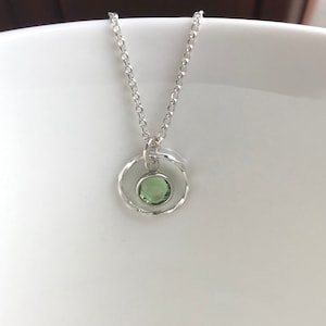May include: A silver necklace with a delicate chain and a pendant featuring a green gemstone set in a circle of twisted silver.