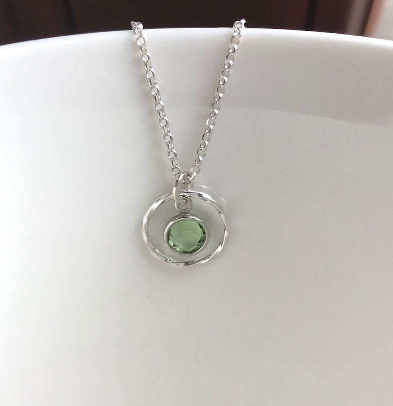 May include: A silver necklace with a delicate chain and a pendant featuring a green gemstone set in a circle of twisted silver.