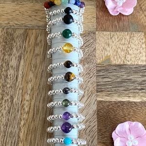May include: A set of silver rings with different colored gemstones. The rings are stacked on a silver ring mandrel. The gemstones include amethyst, turquoise, green aventurine, black onyx, tiger's eye, citrine, malachite, lapis lazuli, and green aventurine.