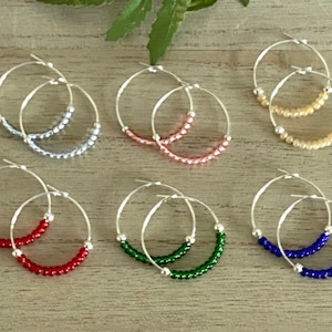 May include: Six pairs of silver hoop earrings with different coloured beads. The beads are in the colours of silver, pink, cream, red, green, and blue.