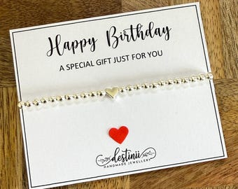 May include: A silver bracelet with a small heart charm on a white card with the text "Happy Birthday A Special Gift Just For You" and the text "destinil handmade jewellery".