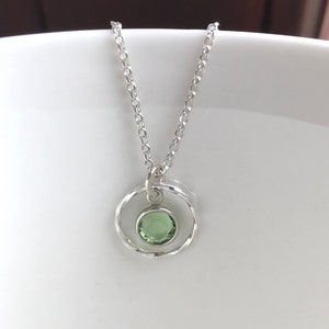 May include: A silver necklace with a delicate chain and a pendant featuring a green gemstone set in a circle of silver.