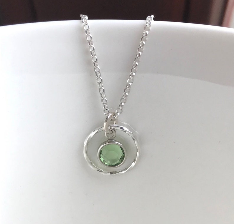 May include: A silver necklace with a delicate chain and a pendant featuring a green gemstone set in a circle of silver.