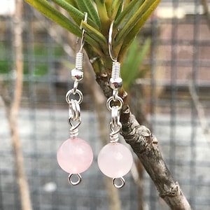 May include: A pair of silver earrings with pink rose quartz beads. The earrings are hanging from a branch.