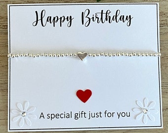 May include: A white card with the text "Happy Birthday" and "A special gift just for you". A silver bracelet with a silver heart charm is on the card. A red heart is below the text. Two white paper flowers with silver centers are on the card.