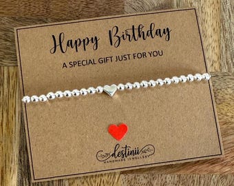 May include: A silver beaded bracelet with a small silver heart charm. The bracelet is displayed on a brown card with the text "Happy Birthday A Special Gift Just For You" and the logo "destinii Handmade Jewellery".