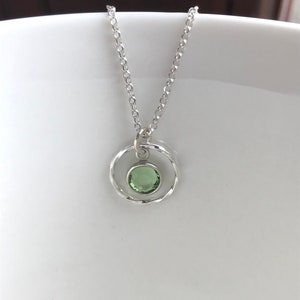 May include: A silver necklace with a delicate chain and a pendant featuring a green gemstone set in a twisted silver circle.
