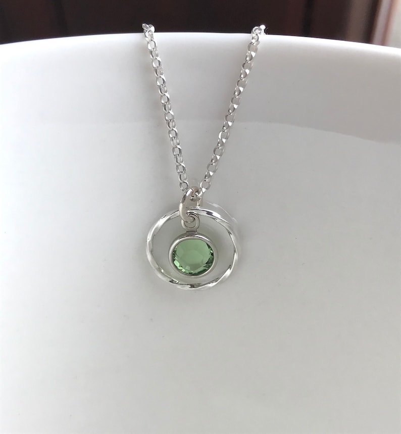 May include: A silver necklace with a delicate chain and a pendant featuring a green gemstone set in a twisted silver circle.