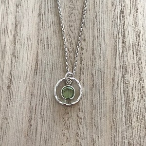 May include: A silver chain necklace with a pendant featuring a green gemstone set in a silver circle.