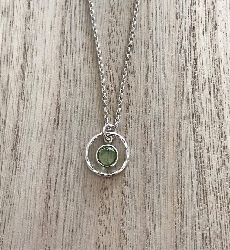 May include: A silver chain necklace with a pendant featuring a green gemstone set in a silver circle.