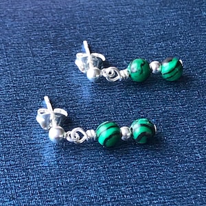 Op de afbeelding: Een paar zilveren oorbellen met groene malachiet kralen. De oorbellen zijn gemaakt in een eenvoudig ontwerp en hebben twee kralen per oorbel.