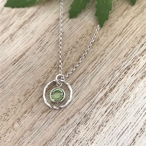 May include: A silver chain necklace with a small, round pendant. The pendant features a green gemstone set in a textured silver circle.