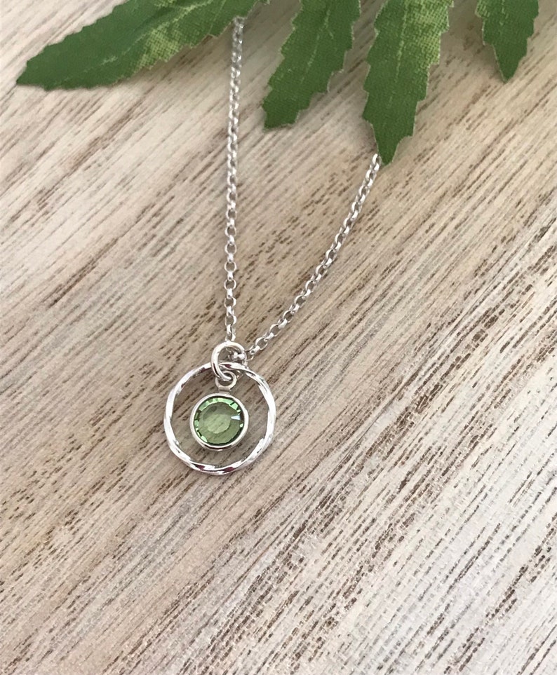 May include: A silver chain necklace with a small, round pendant. The pendant features a green gemstone set in a textured silver circle.