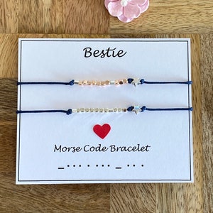 May include: Two friendship bracelets with silver and rose gold beads and star charms on a white card with the text "Bestie" and "Morse Code Bracelet" with the morse code for "Bestie" underneath.