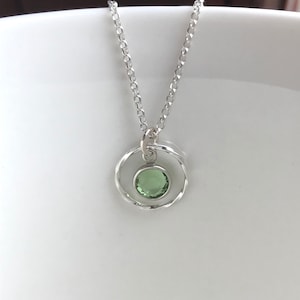 May include: A silver necklace with a delicate chain and a pendant featuring a green gemstone set in a twisted circle.