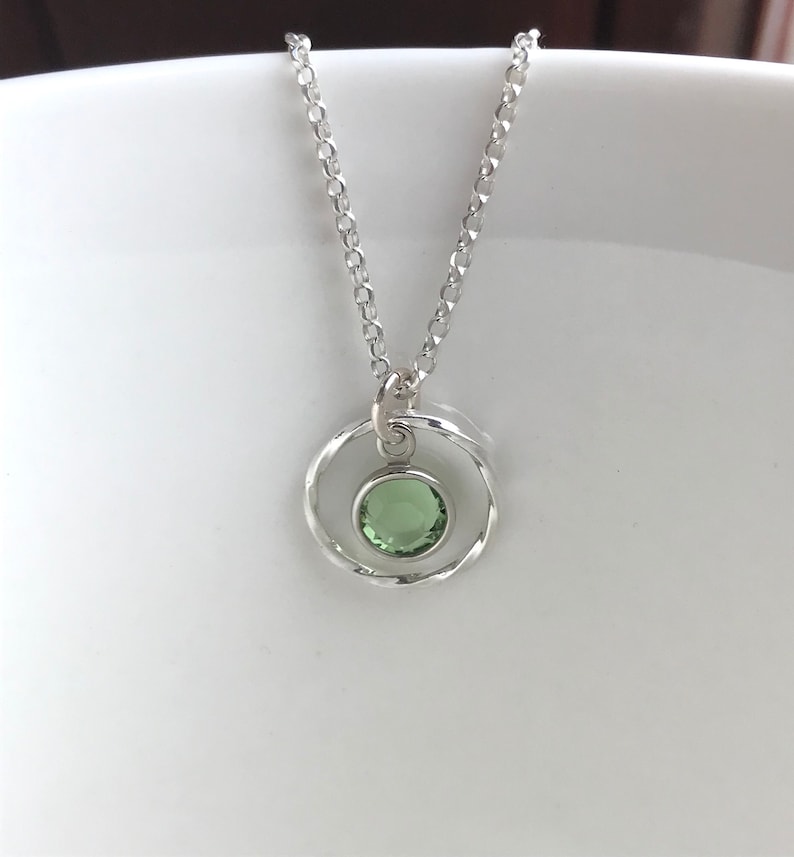May include: A silver necklace with a delicate chain and a pendant featuring a green gemstone set in a twisted circle.