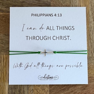 Könnte beinhalten: Eine weiße Karte mit dem Text "Philipper 4,13" und "Ich kann alles tun DURCH CHRISTUS." Ein grünes Schnurarmband mit einem silbernen Kreuzanhänger wird gezeigt. Die Karte lautet auch "Mit Gott sind alle Dinge möglich."