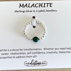 May include: A silver ring with a green malachite stone. The ring is made of small silver beads. The card reads "Malachite Sterling Silver & Crystal Jewellery" and "Malachite is a stone for transformation. Whether you need help with your career, relationships, self-confidence, creativity; Malachite has the properties to address them all! destini HANDMADE JEWELLERY"