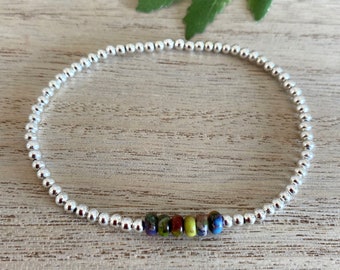May include: A silver beaded bracelet with a row of colorful glass beads in the center.