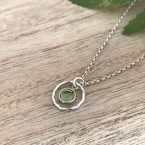 May include: A silver necklace with a delicate circle pendant featuring a small green gemstone.