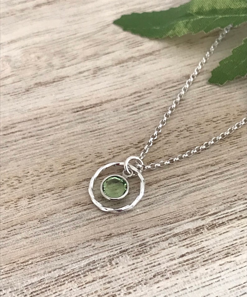 May include: A silver necklace with a delicate circle pendant featuring a small green gemstone.