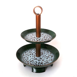 May include: A two-tiered serving stand with a copper-coloured central support and handle. The two circular trays are dark green with a speckled pattern of white, brown, and light blue. The stand has a decorative base.