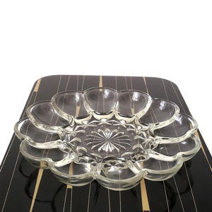 Könnte beinhalten: Klarer Servierteller aus Glas mit gewelltem Rand. Die Schale hat ein zentrales Sternmuster und steht auf einer schwarz-gold gemusterten Oberfläche. Ideal zum Servieren von Vorspeisen oder Snacks.