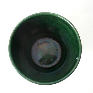 May include: A top-down view of a cylindrical ceramic pot featuring a deep forest green glaze with a glossy finish. The interior base is dark with subtle iridescent highlights and three small, evenly spaced circular indentations.