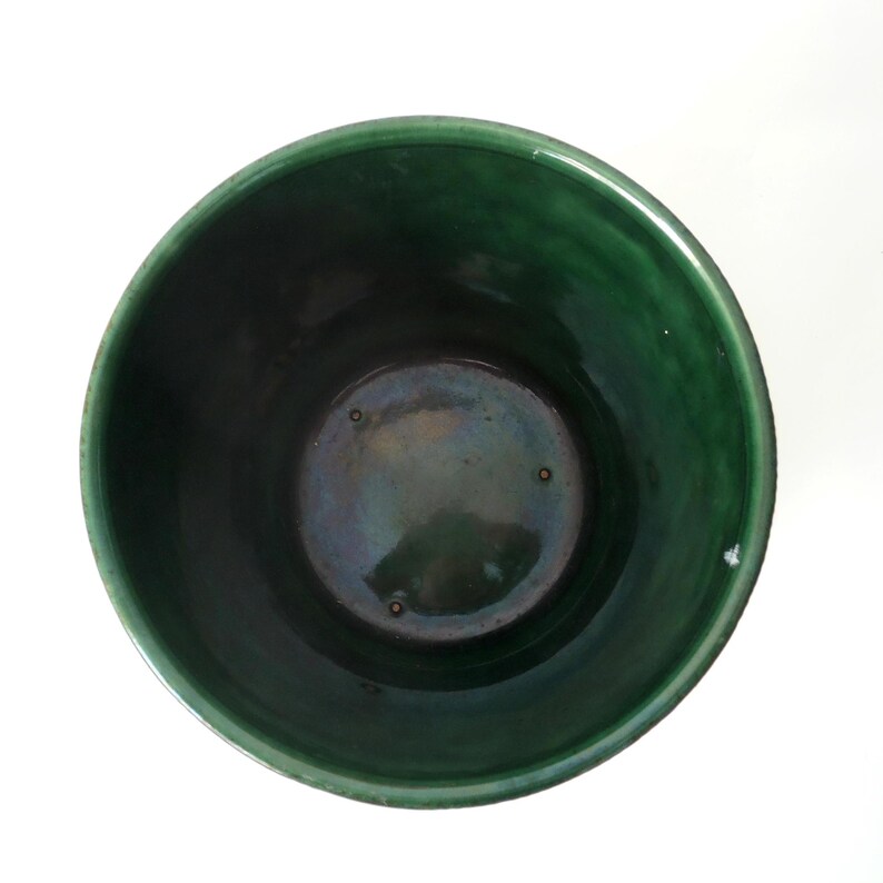 May include: A top-down view of a cylindrical ceramic pot featuring a deep forest green glaze with a glossy finish. The interior base is dark with subtle iridescent highlights and three small, evenly spaced circular indentations.