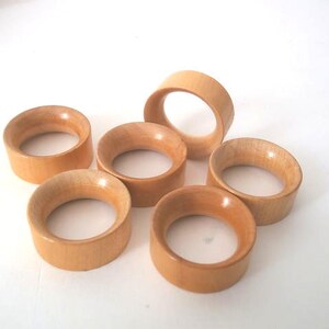 May include: Six wooden napkin rings in a light brown colour. The rings are stacked on top of each other.