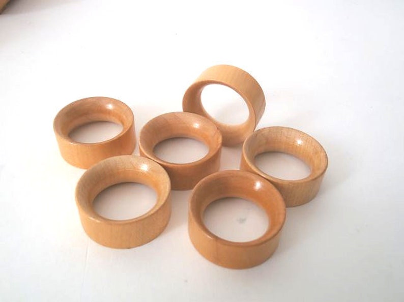 May include: Six wooden napkin rings in a light brown colour. The rings are stacked on top of each other.