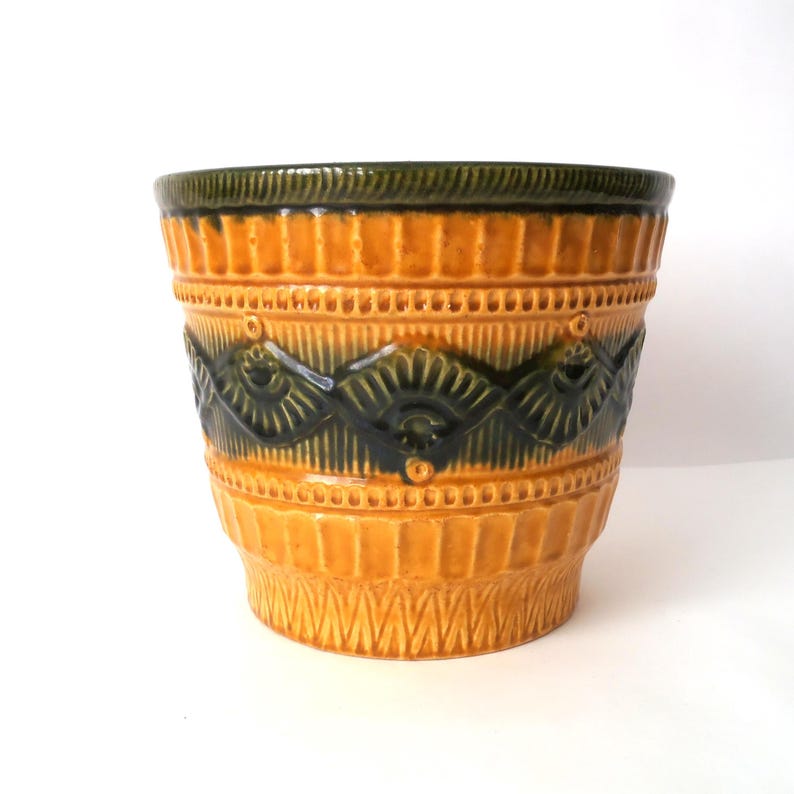 May include: A ceramic planter featuring a vibrant mustard yellow glaze with a dark forest green rim and a repeating embossed pattern of stylized fan shapes and vertical lines encircling the exterior of the cylindrical vessel.