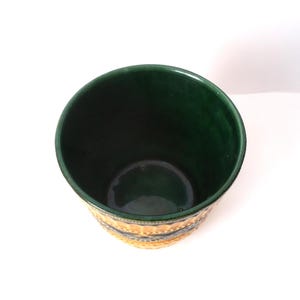 May include: A cylindrical ceramic planter with a deep forest green interior and a glossy finish. The exterior features a textured pattern with alternating bands of yellow and dark green, showcasing a repeating embossed geometric design.