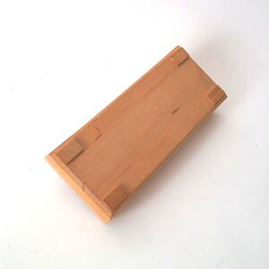 May include: A wooden box with a light brown finish and four small feet on the bottom.