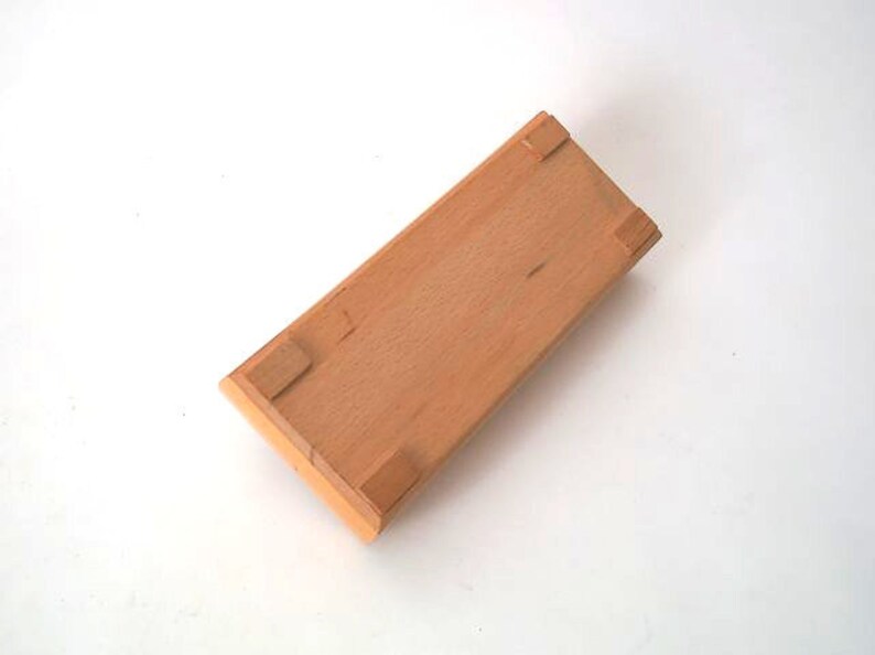May include: A wooden box with a light brown finish and four small feet on the bottom.