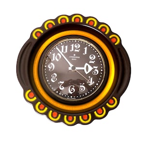 May include: A vintage wall clock with a dark brown scalloped frame and a black face. The clock features white numerals and hands, with a yellow and orange accent ring. The clock face reads "Junghans Quartz".