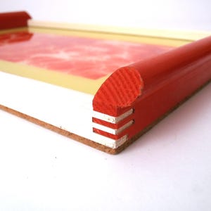 May include: A red and white tray with a rounded edge. The tray is made of wood and has a white interior.