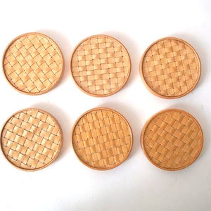 May include: Six round woven coasters in a light brown colour. The coasters have a woven pattern and are made of natural materials.