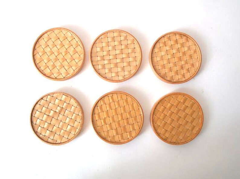 May include: Six round woven coasters in a light brown colour. The coasters have a woven pattern and are made of natural materials.
