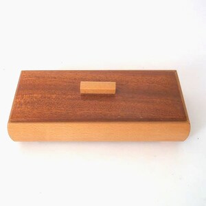May include: A rectangular wooden box with a light brown lid and a dark brown base. The lid has a small rectangular wooden knob.