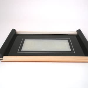 May include: A black tray with a wooden frame and black trim. The tray has a clear glass insert with a black border.