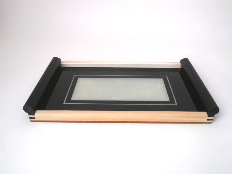 May include: A black tray with a wooden frame and black trim. The tray has a clear glass insert with a black border.