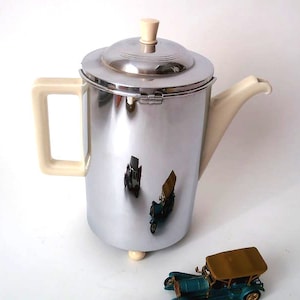 Peut inclure: Une cafetière en argent et crème avec un corps arrondi et une poignée et un bec verseur crème. La cafetière a une surface brillante et réfléchissante.