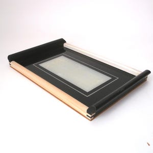 May include: A black tray with a wooden frame and a white border around the inside. The tray has rolled edges.